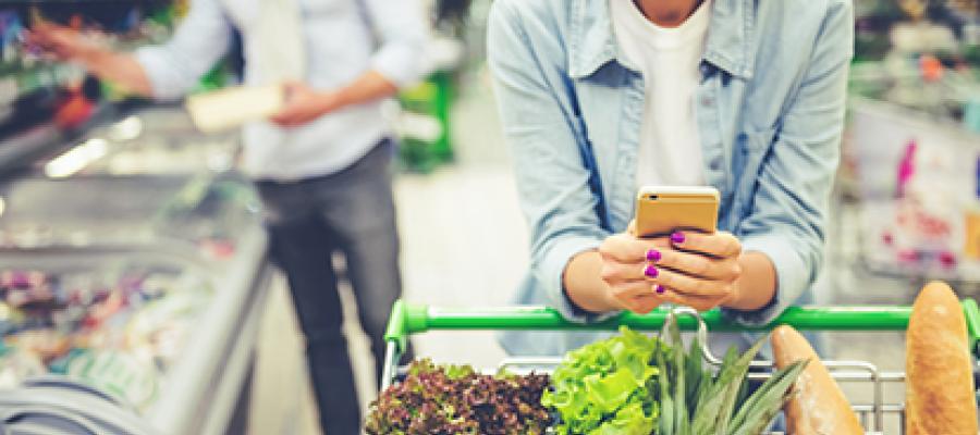 Closeup of woman pushing grocery cart while looking at her phone