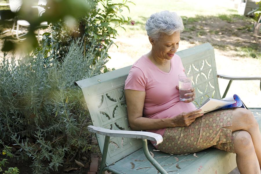Older woman reading a magazine with a glass of water outside