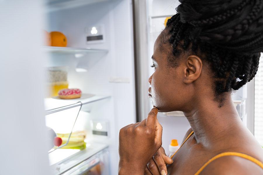 Woman looking into fridge, deciding if she's hungry