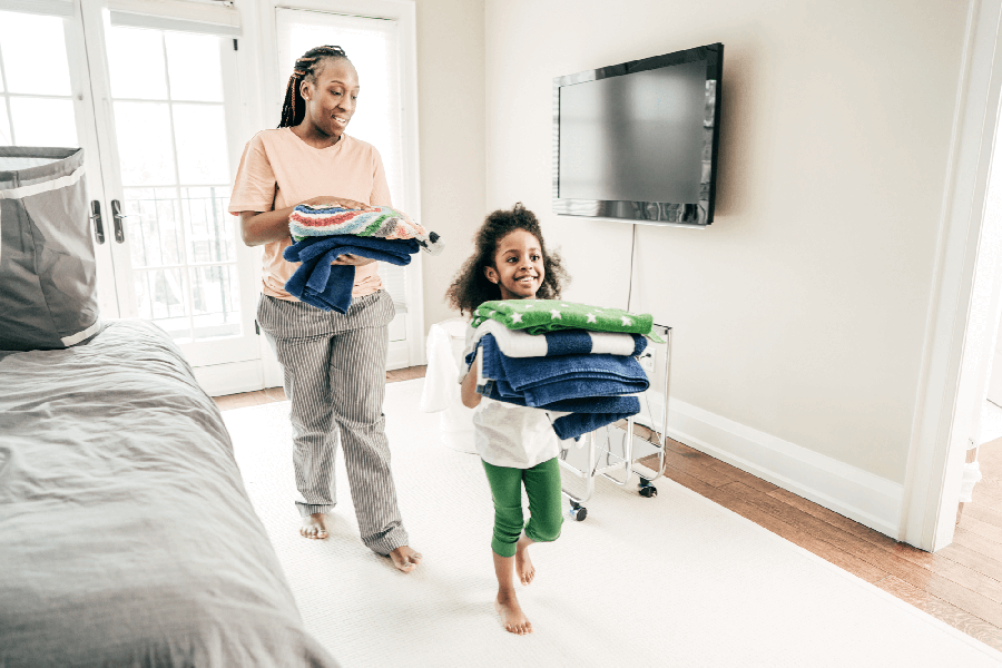 Mother and daughter walking with folded laundry around the house