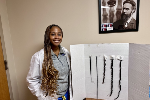 Udongwo with the board showing the five most popular Black hairstyles.